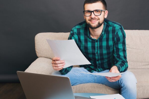 Young hipster handsome bearded man sitting on couch at home