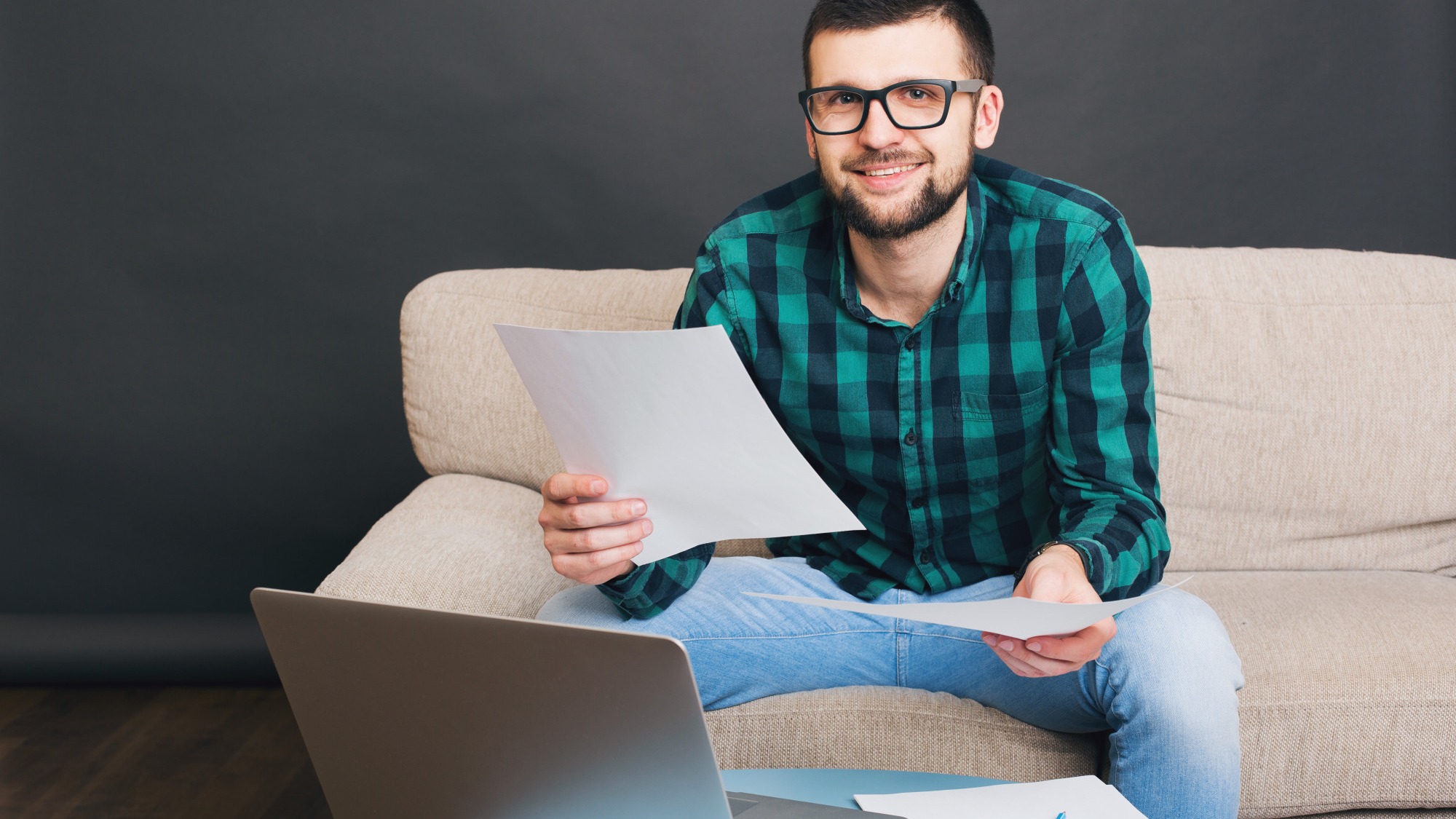 Young hipster handsome bearded man sitting on couch at home