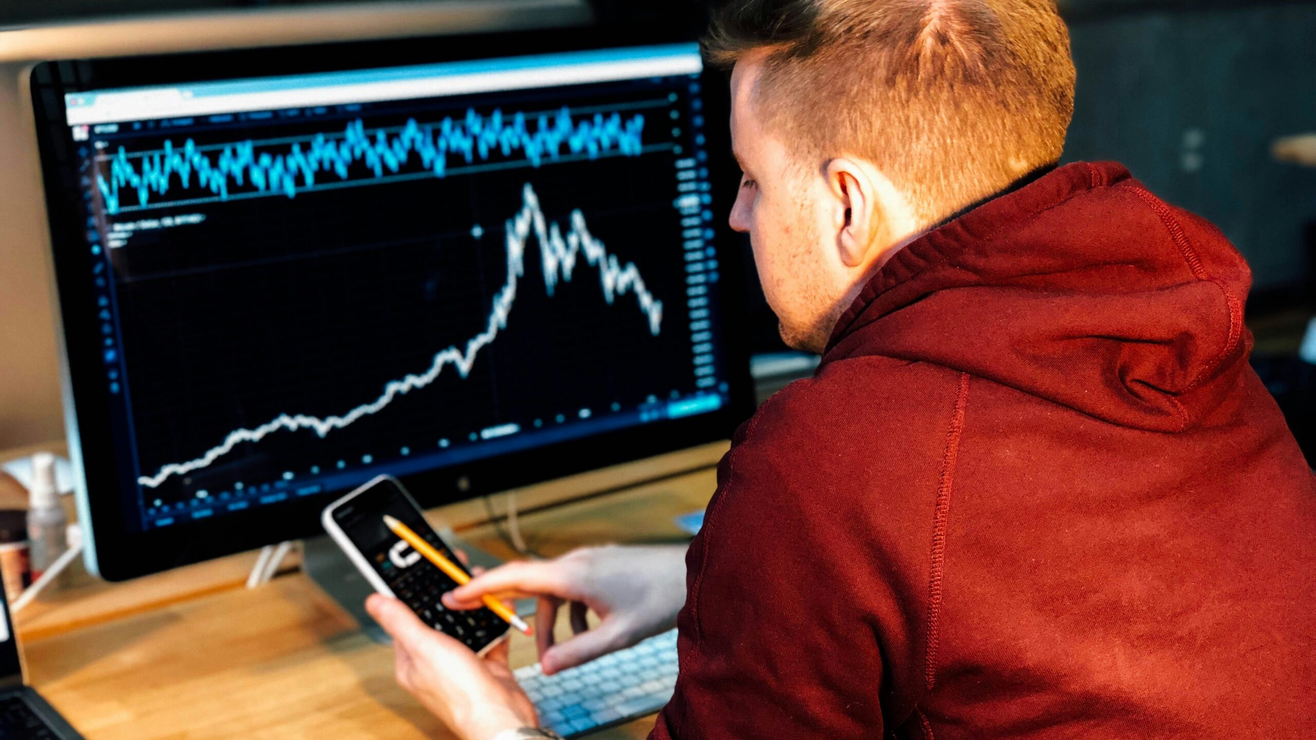man holding black smartphone with flat screen monitor in front