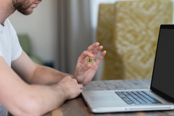 A man sitting at the laptop and holding a bitcoin
