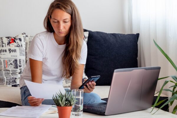 Woman works at home, seats close to Laptop with notebook, glass of water on table in home workspace