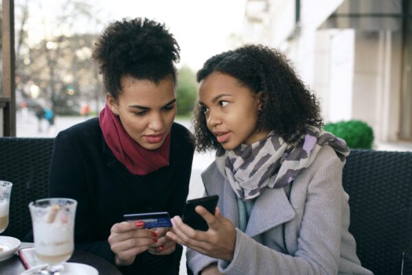 Two women looking at a smartphone with credit card.