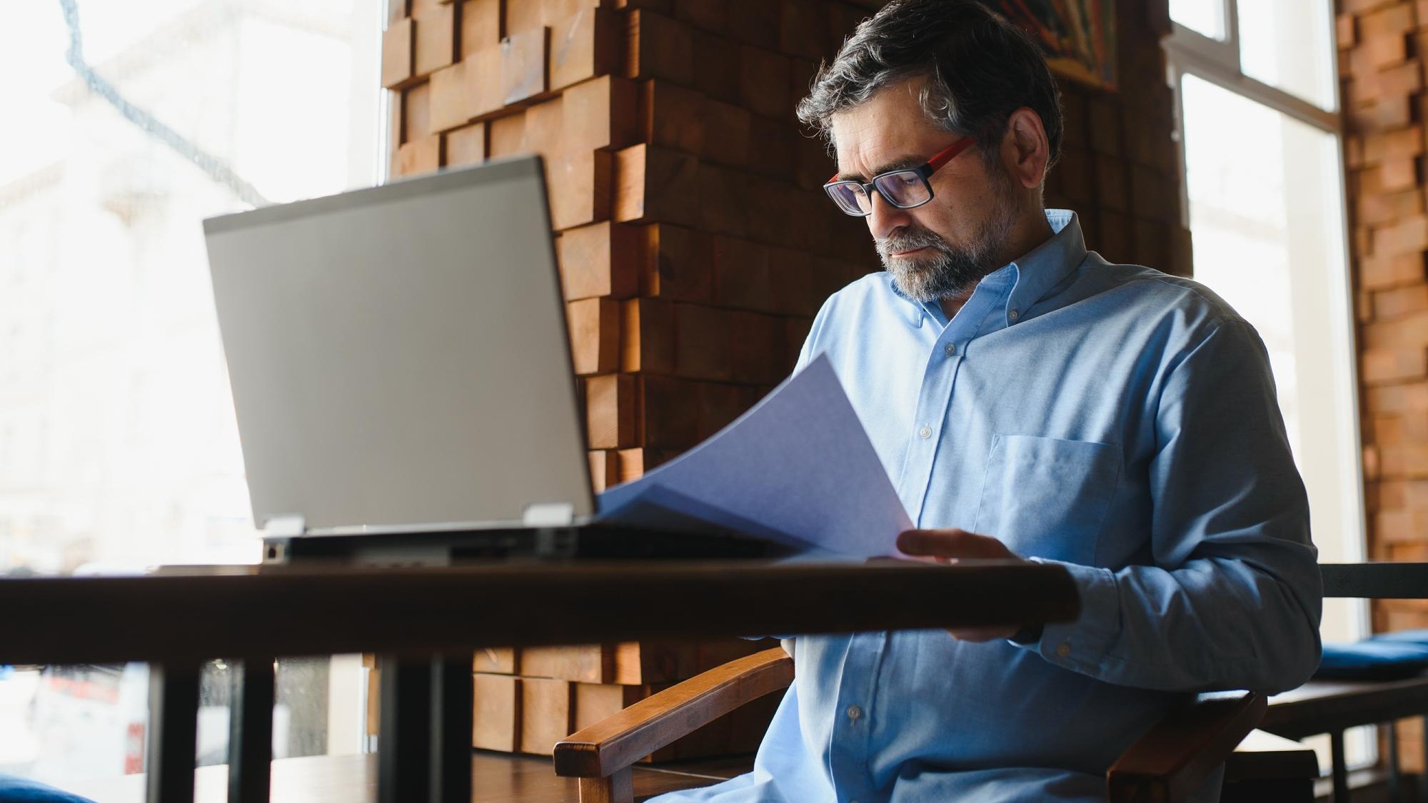 Mature businessman drinking coffee in cafe Portrait of handsome man wearing stylish eyeglasses using laptop looking at camera smiling Coffee break concept