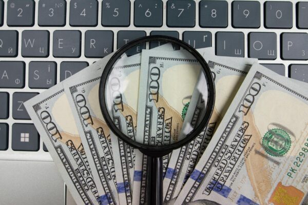 Dollars and a magnifying glass on a laptop keyboard