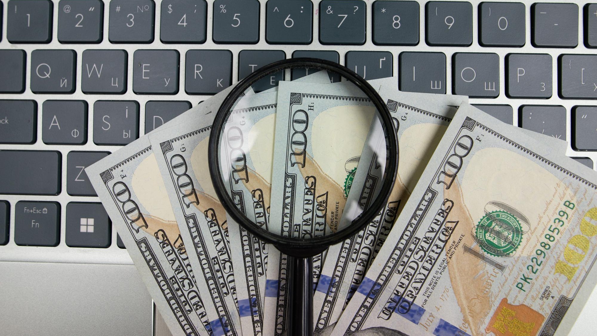 Dollars and a magnifying glass on a laptop keyboard