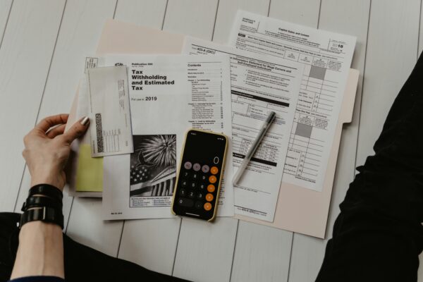 person holding paper near pen and calculator