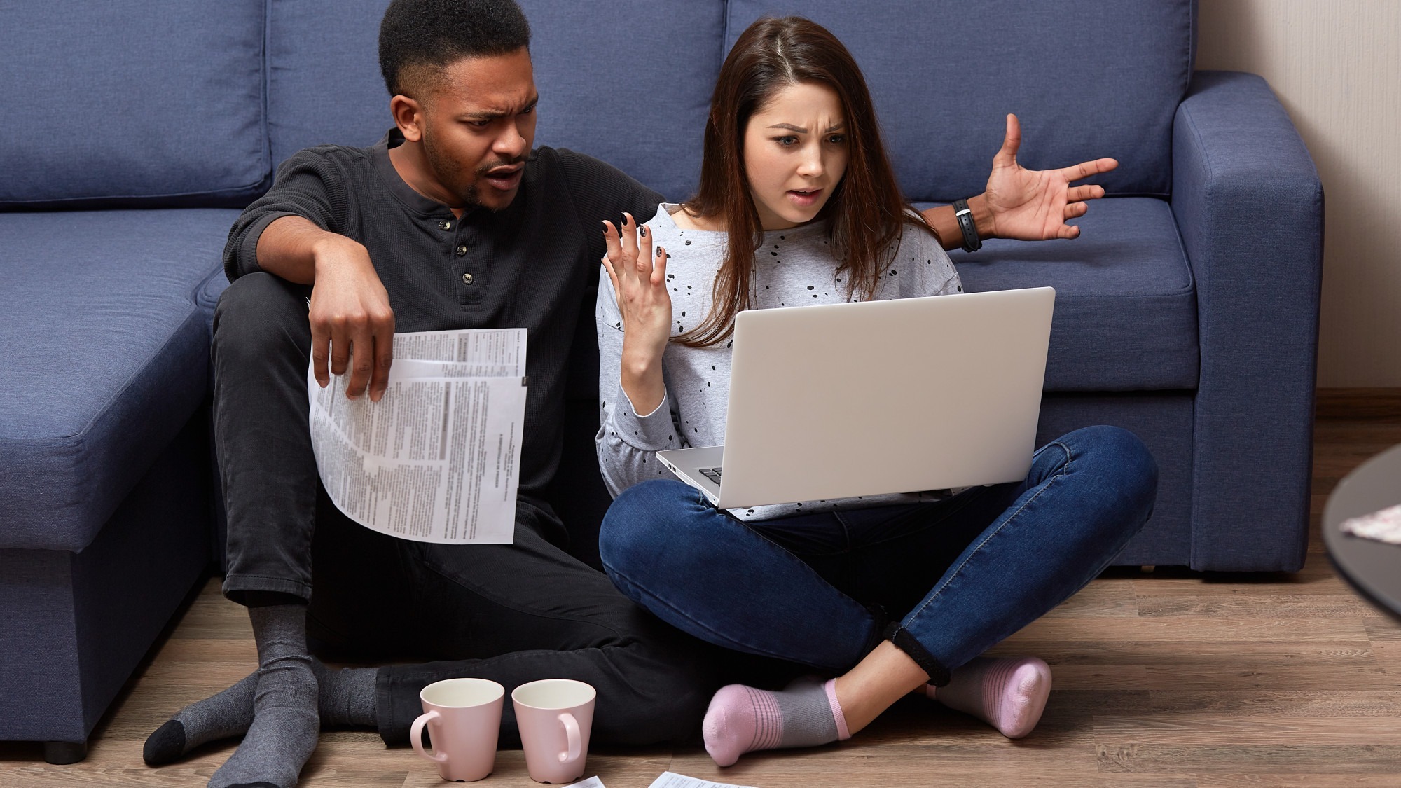 Indoor shot of multicultural couple spending free time at home and checking bills, dressed casually, sitting in front of laptop