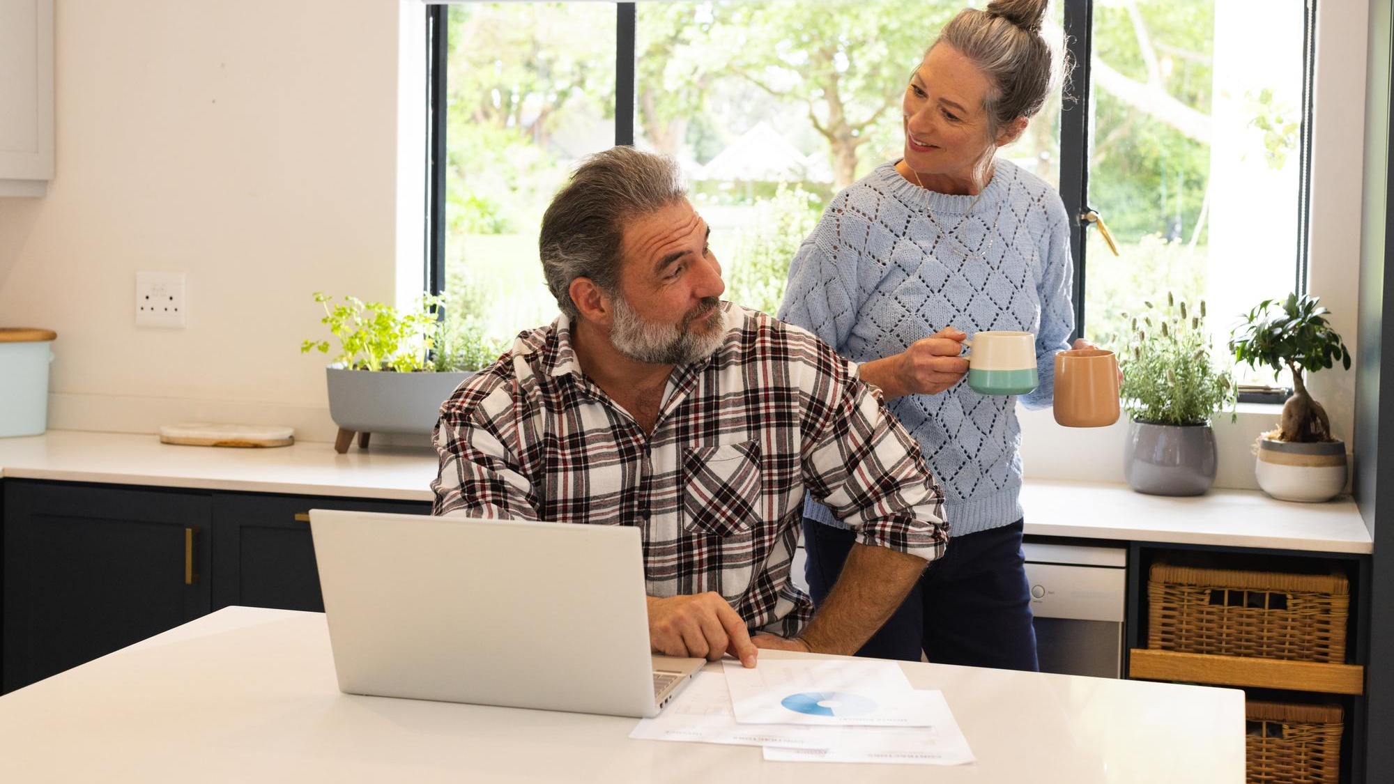 Mature couple enjoying coffee break at home man using laptop in kitchen