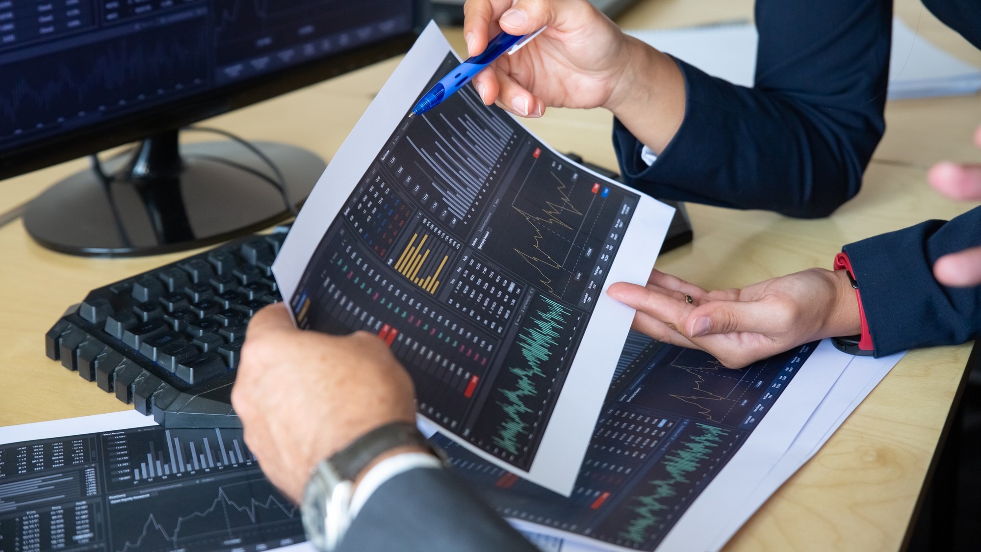 Brokers discussing trading strategy, holding papers with financial data, pointing pen at charts. Cropped shot. Broker job or stock market exchange concept