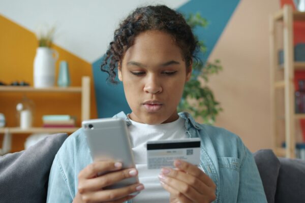 Young woman holding credit card and smartphone indoors