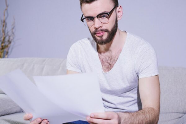 Young bearded business man with glasses working with business papers sitting at home on the couch