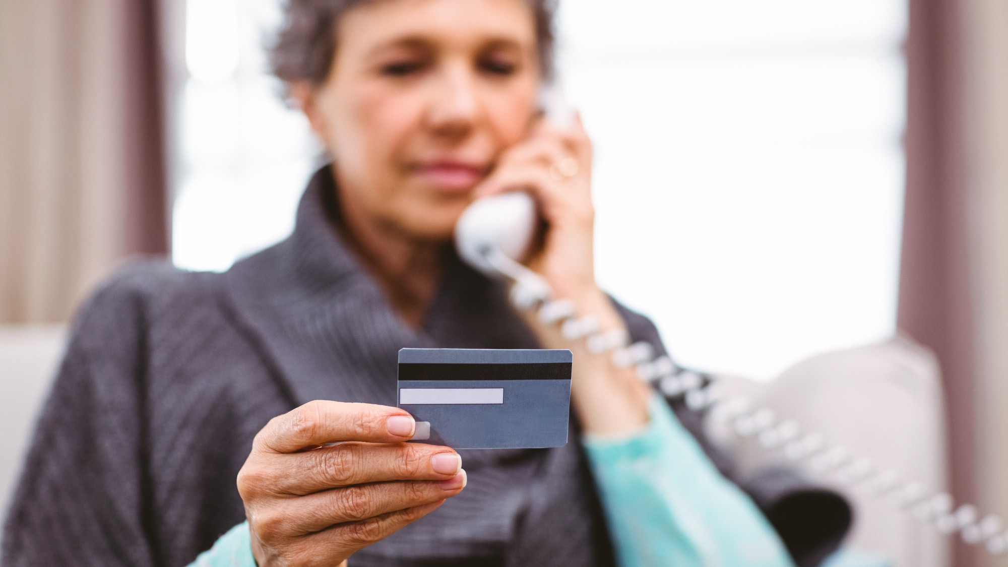 Mature woman holding credit card while talking on telephone