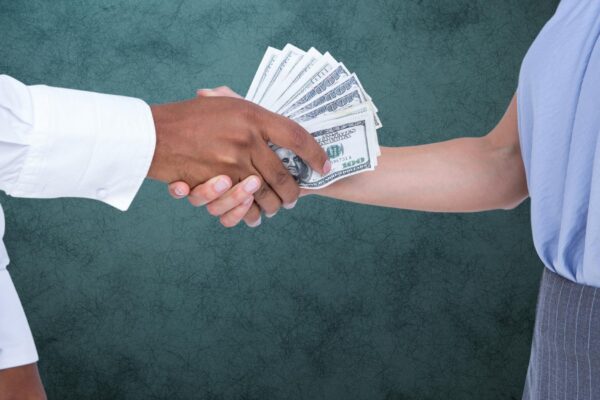 Businessman bribing partner while shaking handsA against teal background