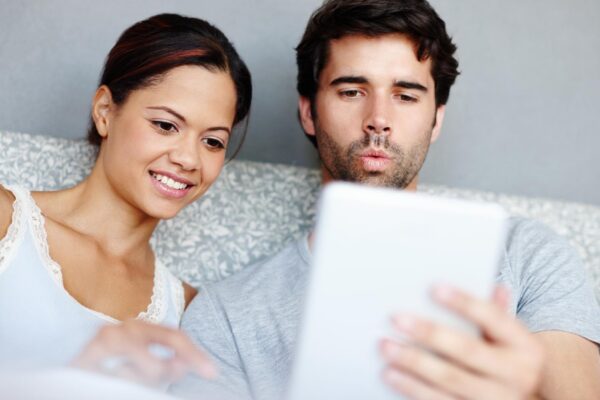 Morning woman and man in bed with tablet reading or online video streaming service in home Relax smile and couple in bedroom with digital app for social media bonding and weekend in apartment