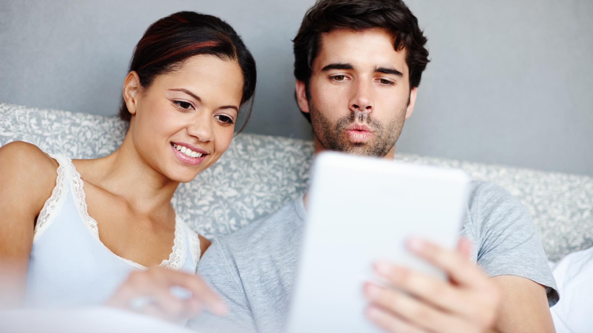Morning woman and man in bed with tablet reading or online video streaming service in home Relax smile and couple in bedroom with digital app for social media bonding and weekend in apartment