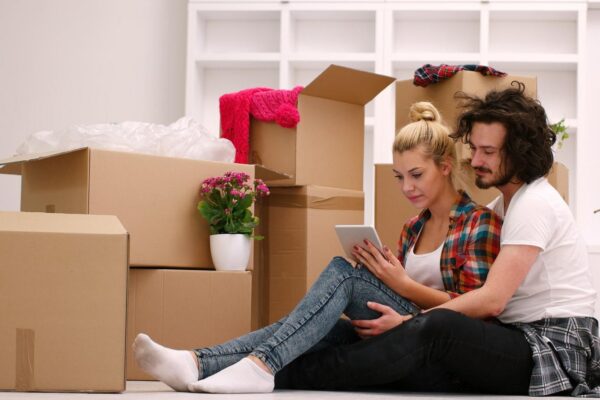 Relaxing in new house. Cheerful young couple sitting on the floor while cardboard boxes laying all around them