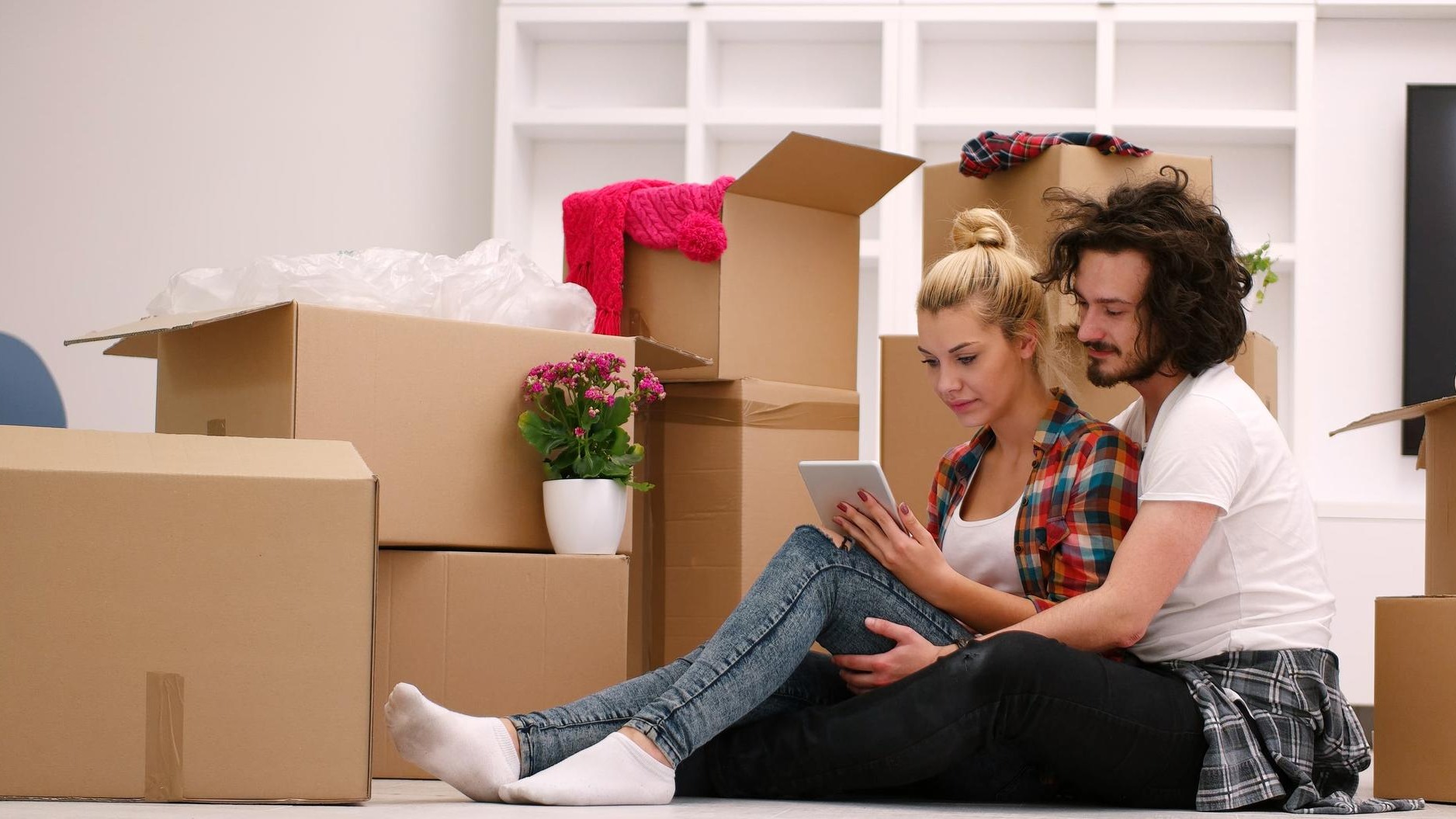 Relaxing in new house. Cheerful young couple sitting on the floor while cardboard boxes laying all around them