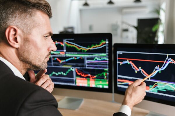 Photo of european businessman 30s wearing suit sitting at table in office and working with graphics and charts on computer
