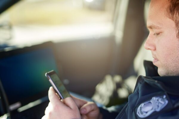 Police officer and man texting with phone in patrol car for security contact law enforcement update and mobile notification Policeman typing message on cellphone for crime news connection and app