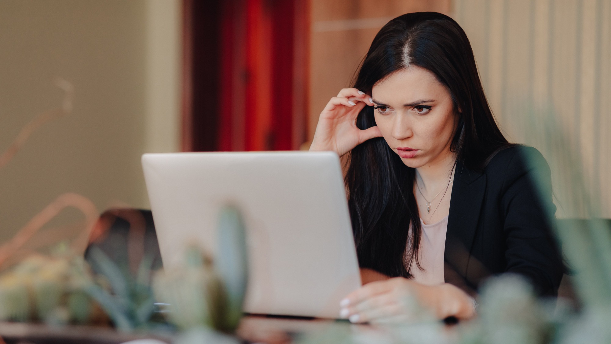Young attractive emotional girl in business-style clothes sitting at a desk on a laptop