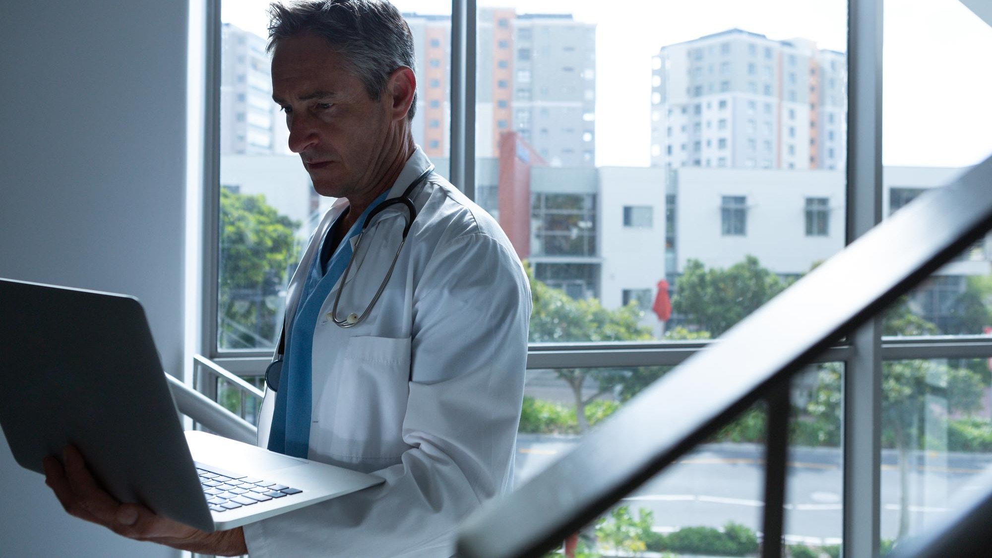 Male doctor using laptop while walking on stairs