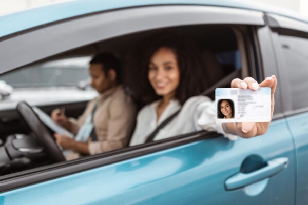 Happy middle eastern woman sitting in car showing driver license