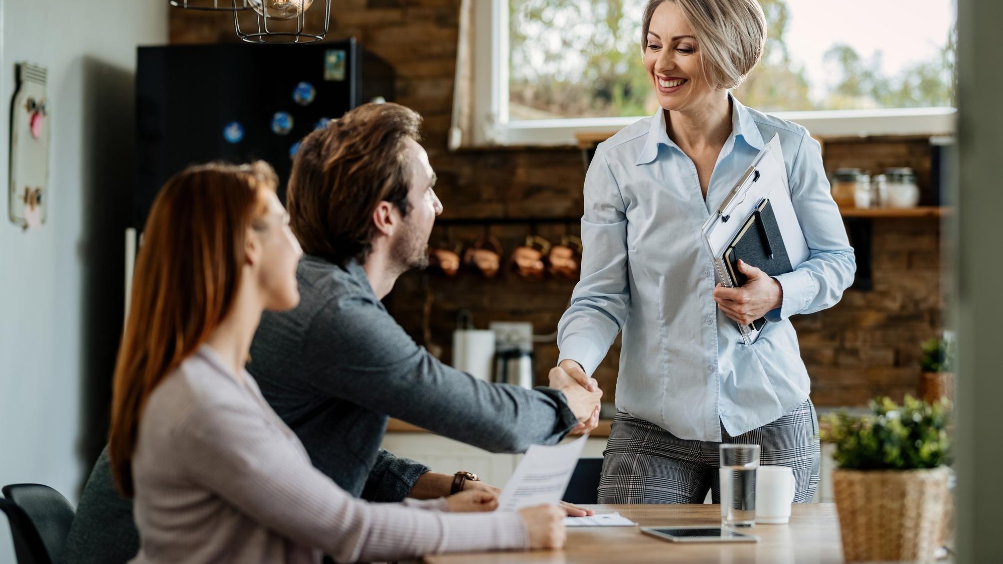 Happy insurance agent meeting with young couple and shaking hands with a man at their home