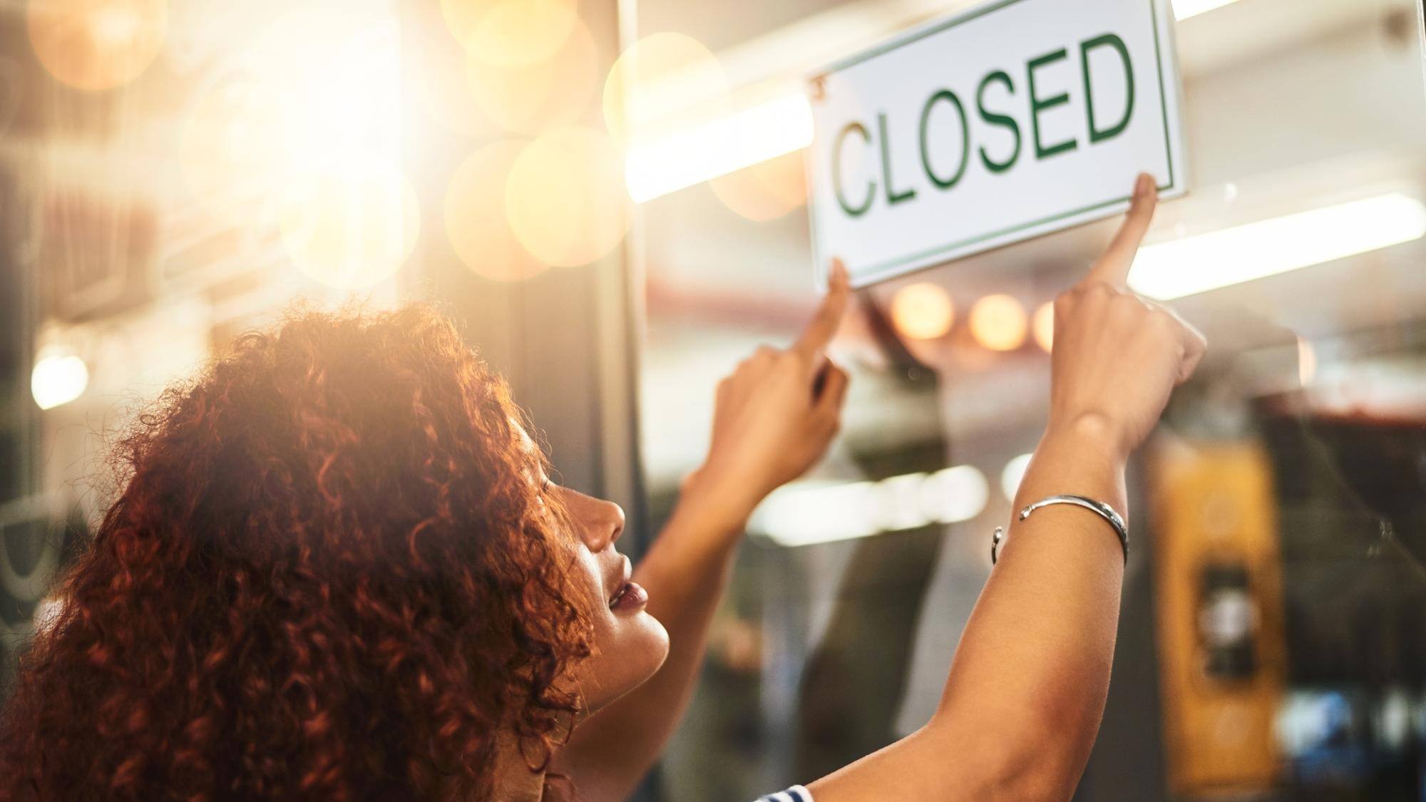 Its the end of another successful day Shot of a young woman hanging up a closed sign in her store