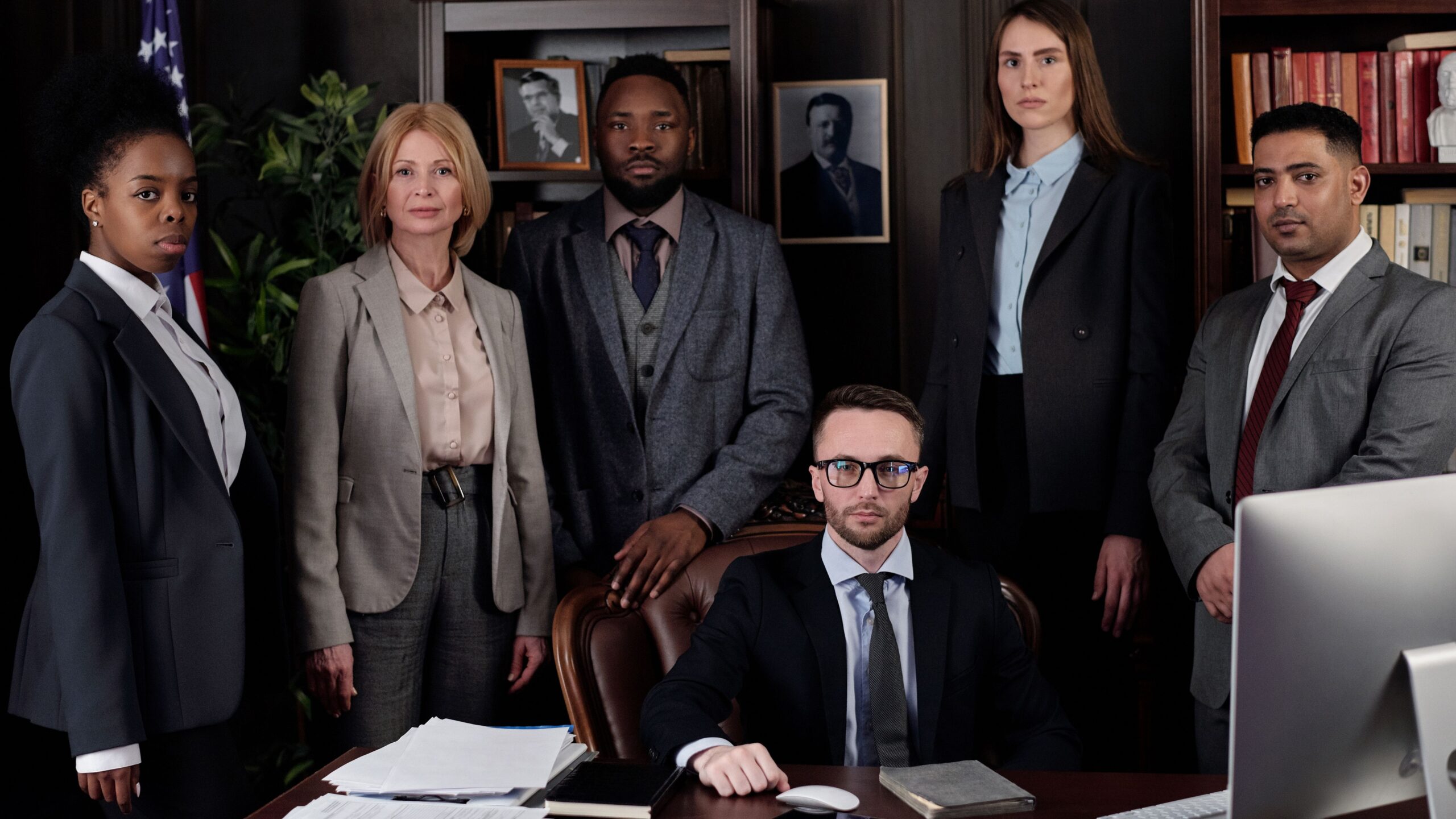A diverse group of business professionals posing in an office, showcasing teamwork and leadership.