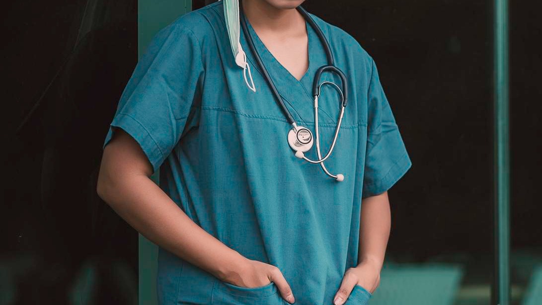 Tired depressed female asian scrub nurse wears face mask blue uniform sits on hospital floorYoung woman doctor stressed from hard work