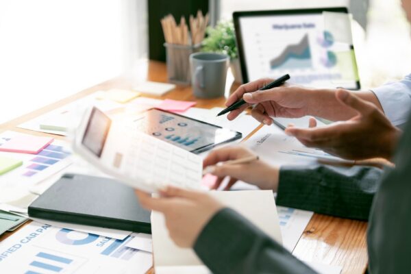 Two business people point to graphs and charts on tablet to analyze data balance sheet account and net profit to plan new sales strategies