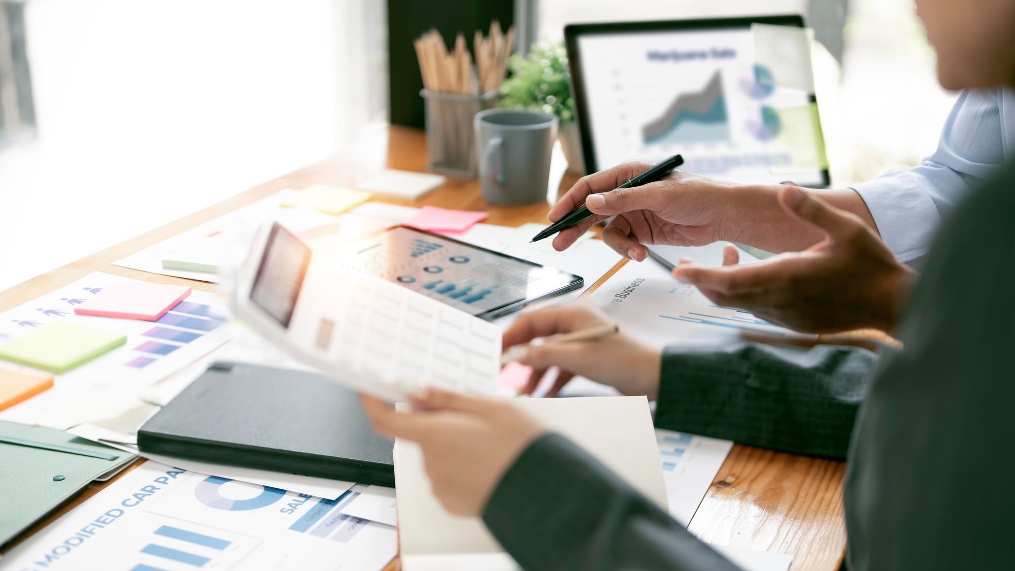 Two business people point to graphs and charts on tablet to analyze data balance sheet account and net profit to plan new sales strategies