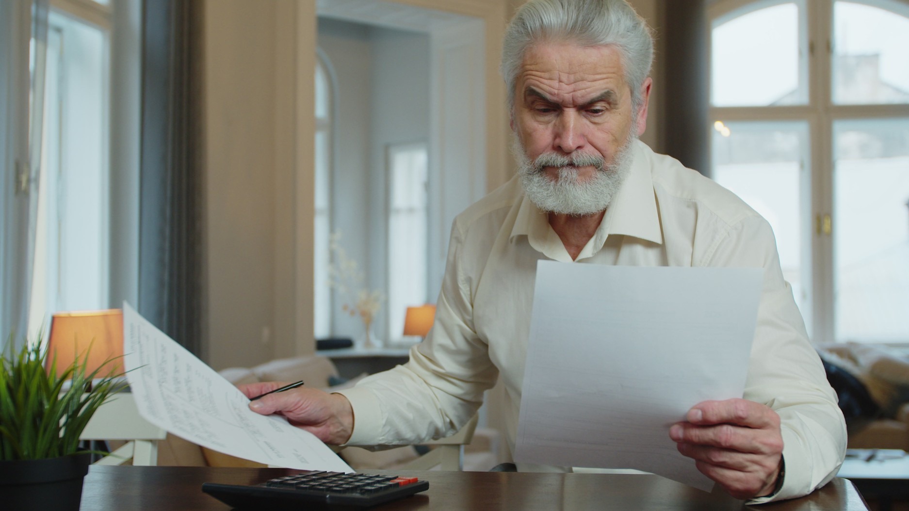 Serious mature man calculating bills, checking finances manage personal finances seated at table at home.