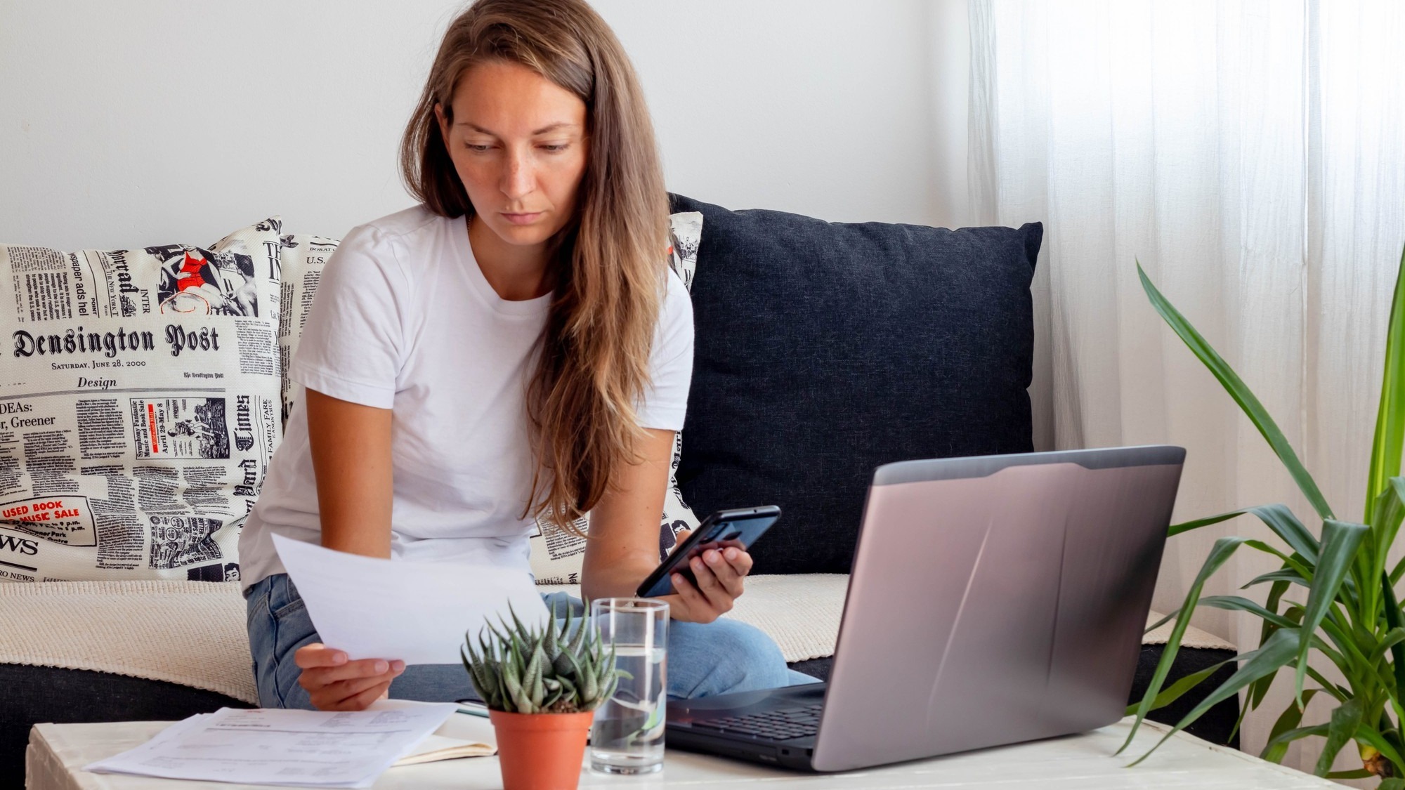 Woman works at home, seats close to Laptop with notebook, glass of water on table in home workspace