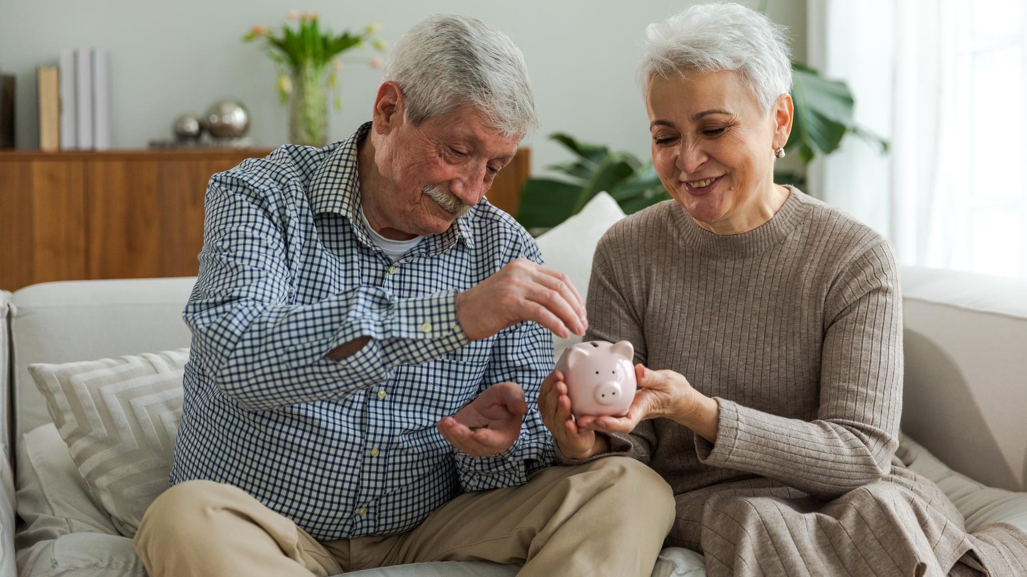 Saving money investment for future senior adult mature couple holding piggy bank putting money coin