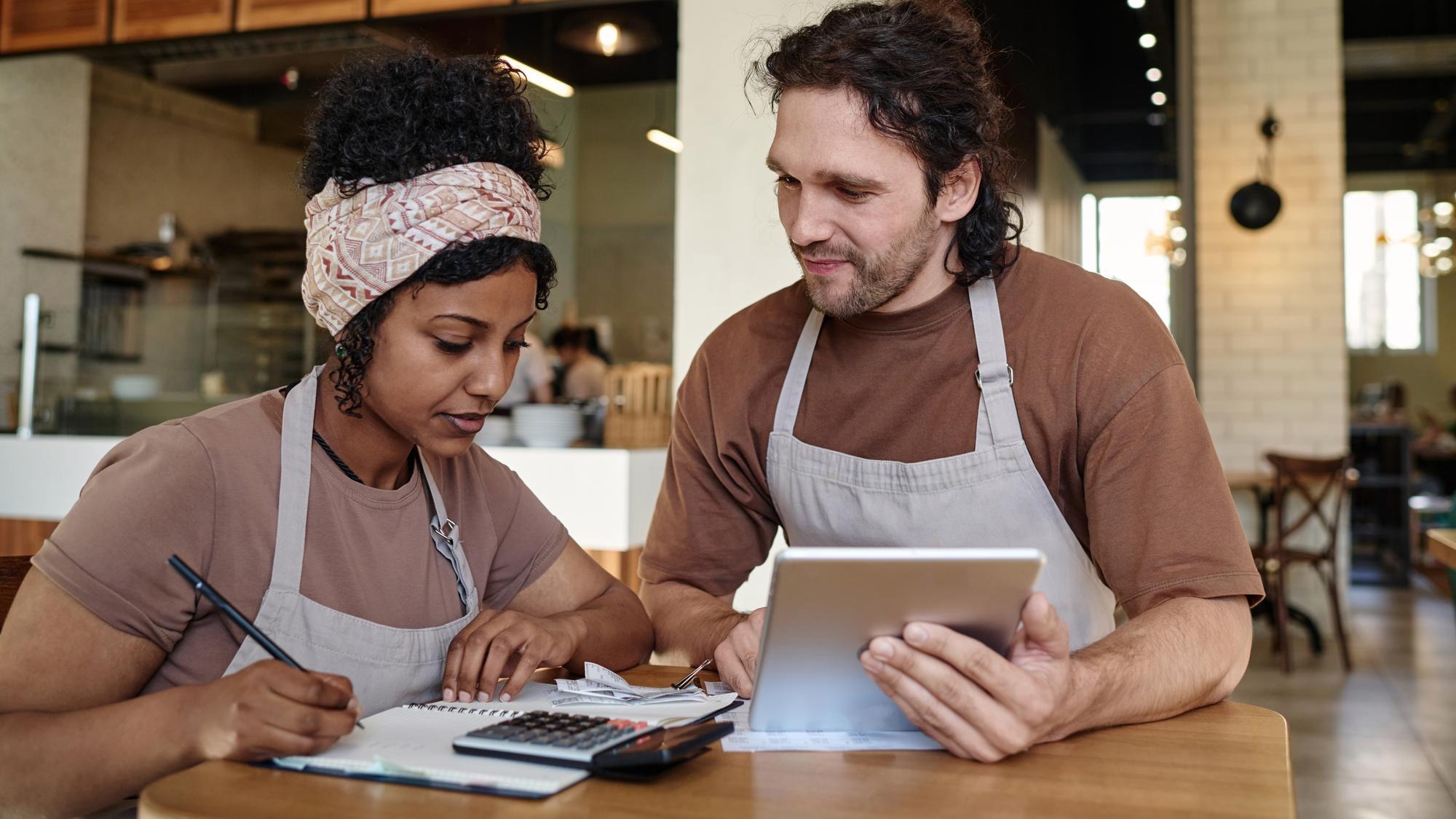 Two biracial eatery workers sitting over income calculation sitting at table after workday
