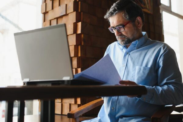 Mature businessman drinking coffee in cafe Portrait of handsome man wearing stylish eyeglasses using laptop looking at camera smiling Coffee break concept