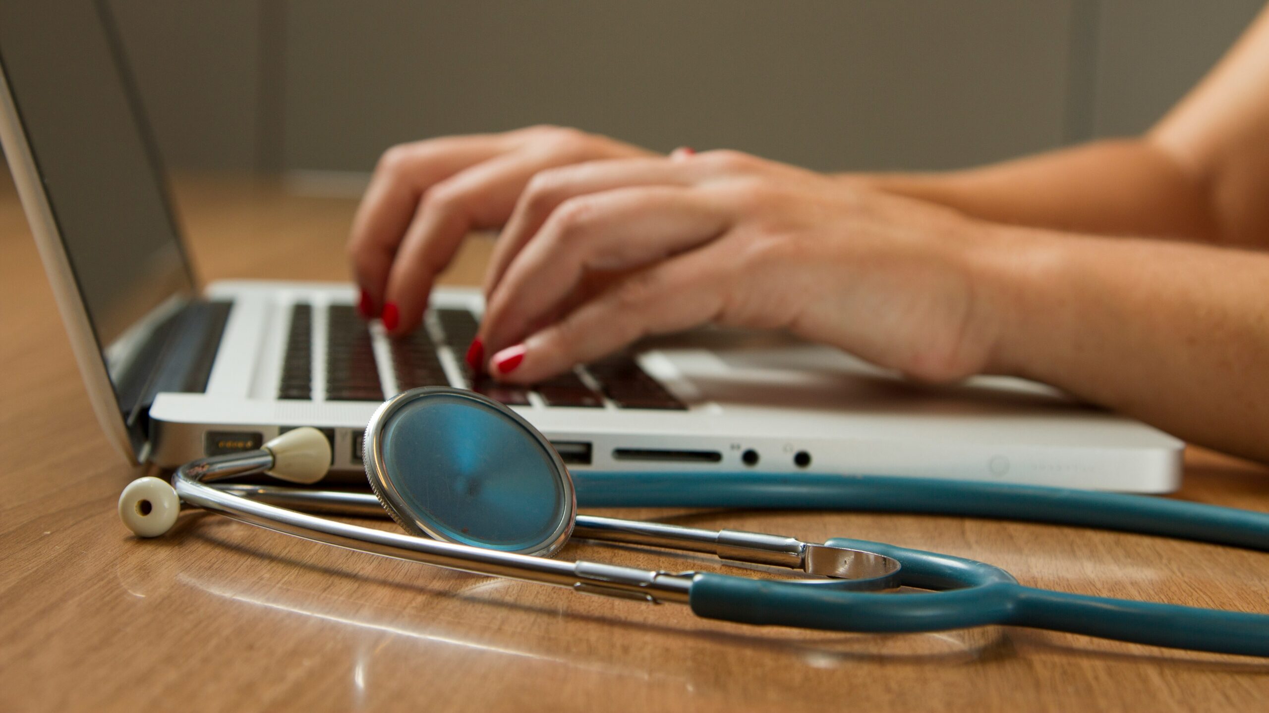 person sitting while using laptop computer and green stethoscope near