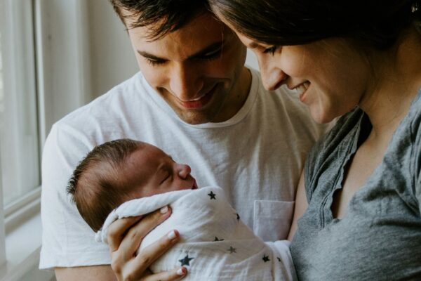 woman holding baby beside man smiling