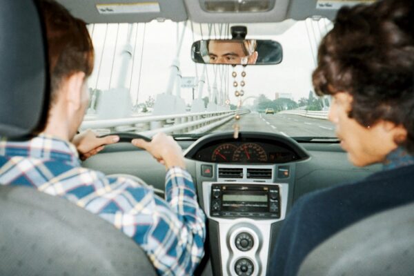 A man driving a car with another man in the back seat