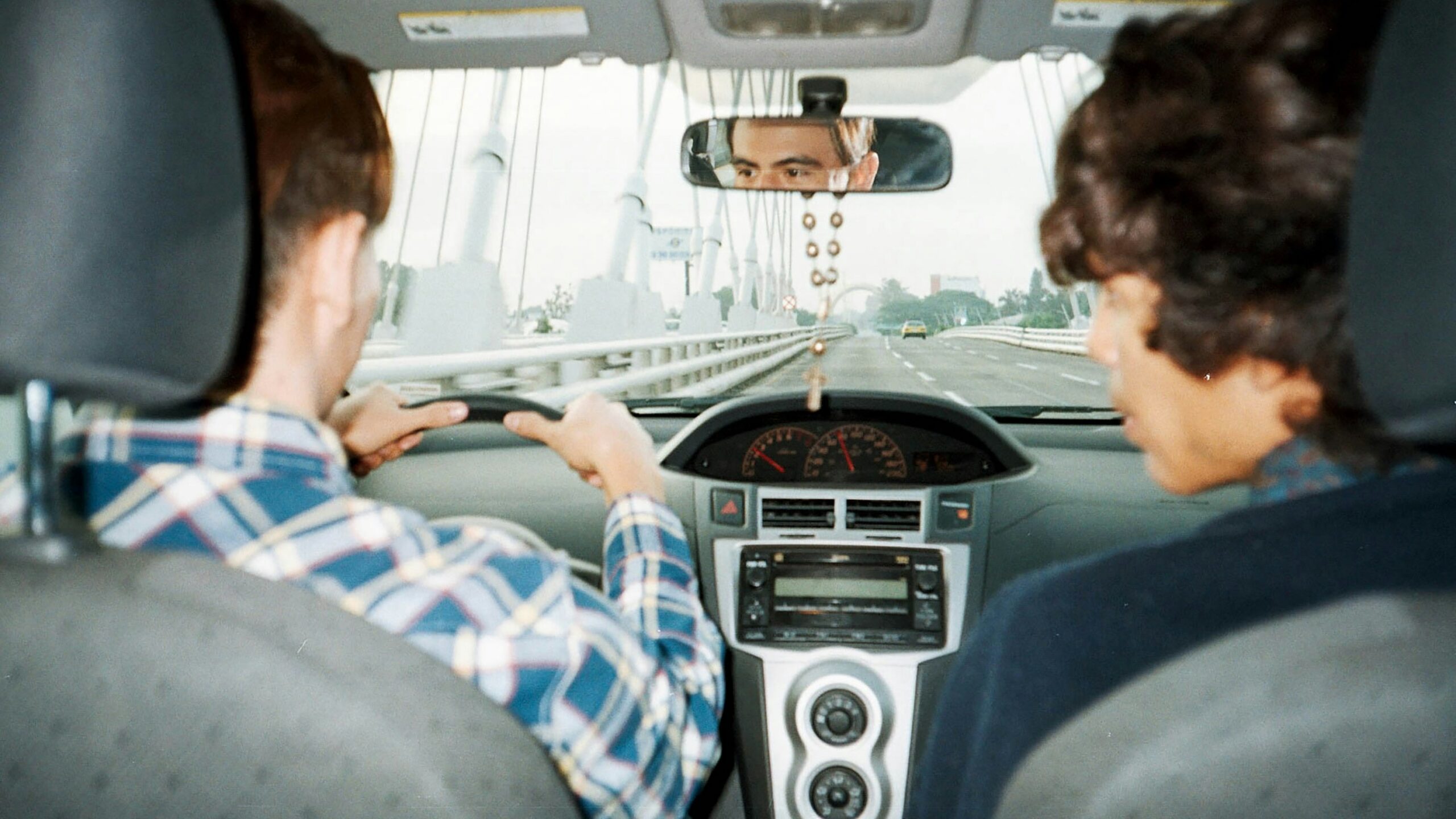 A man driving a car with another man in the back seat