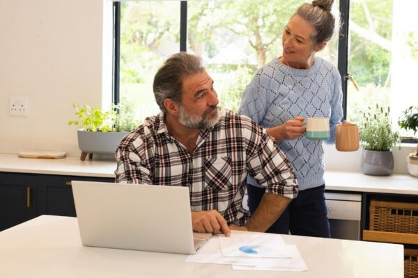 Mature couple enjoying coffee break at home man using laptop in kitchen