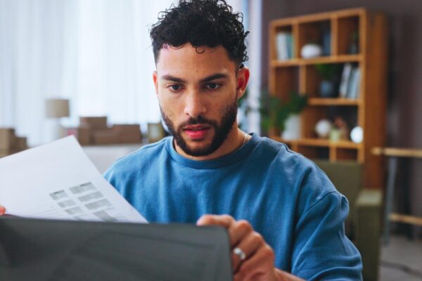 Small business review and man with documents laptop and confused by financial report and online Reading entrepreneur and person with paperwork for taxes boxes and planning for audit or serious