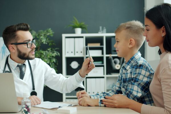 Doctor examines a young boy with his mother present.