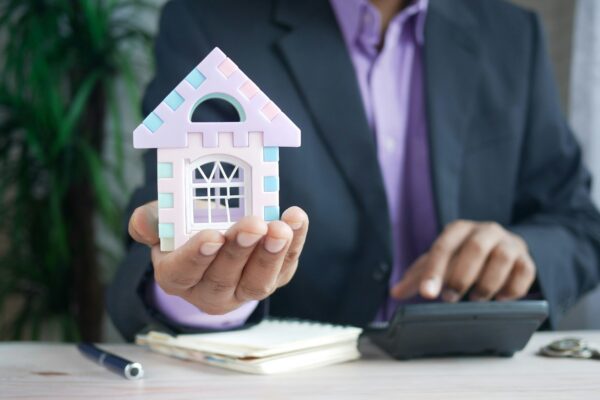 man holding model house at desk with calculator