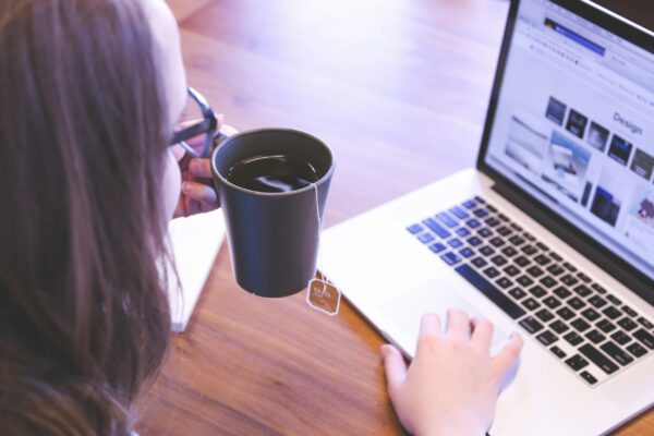 woman holding tea filled mug using MacBook