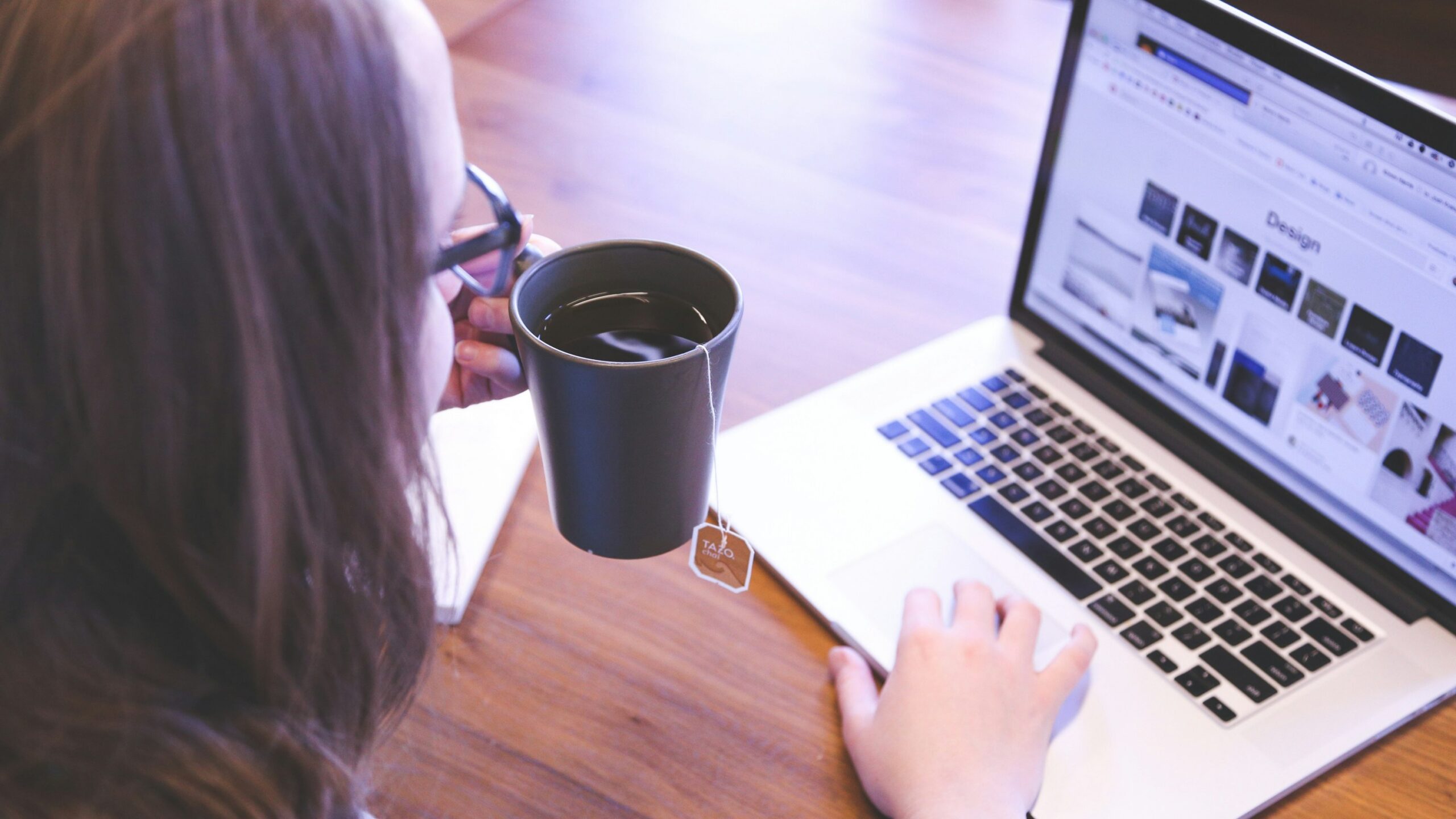 woman holding tea filled mug using MacBook
