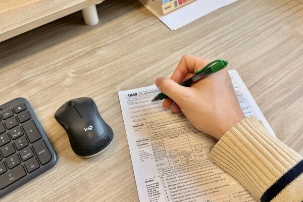 Hand writing on document next to keyboard and mouse.