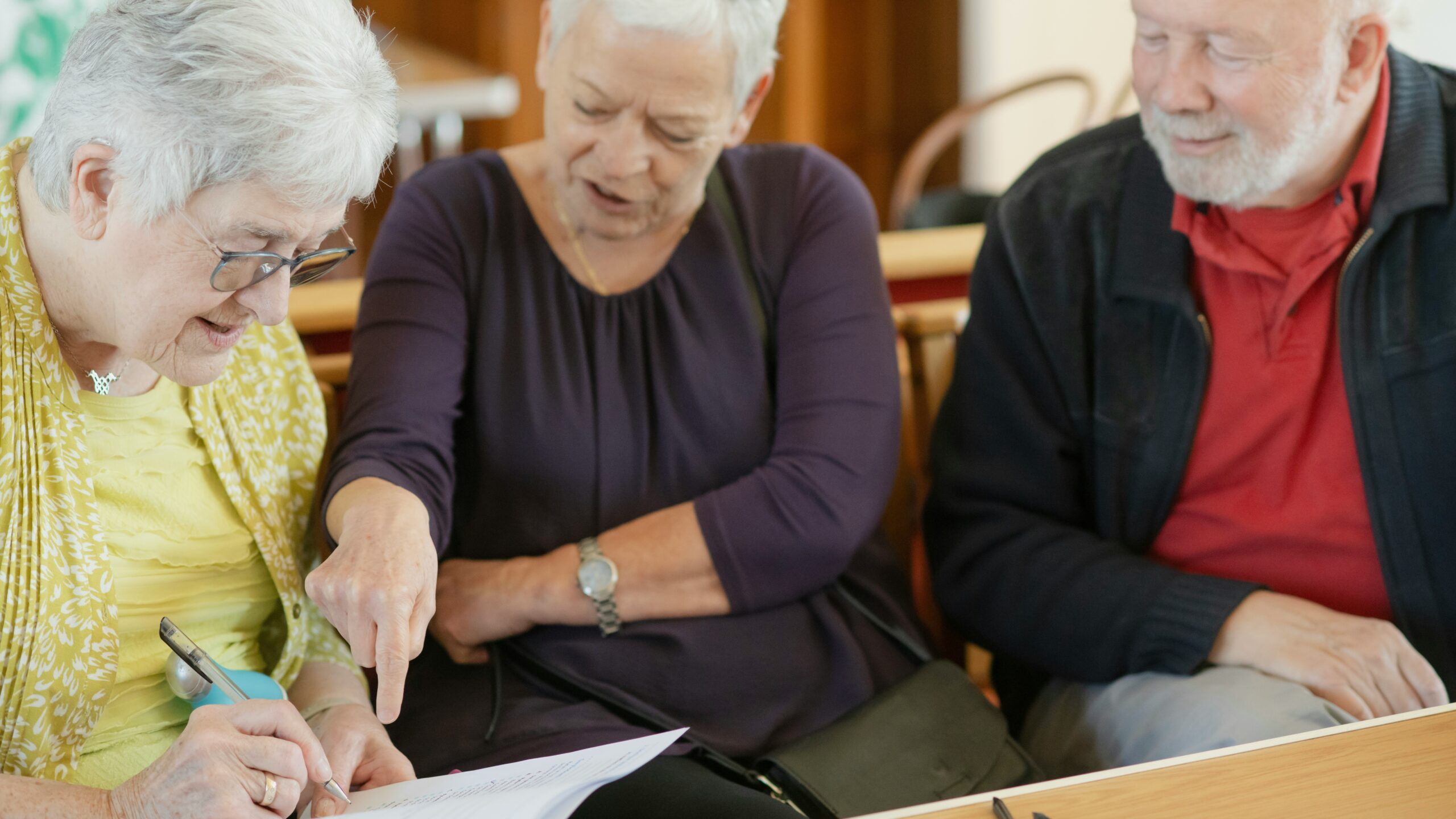 Three older adults are looking at a paper.