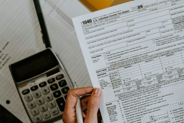 Hands holding tax forms with calculator and laptop.